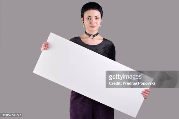 cute short haired young modern woman with short hair in fashionable clothes holding blank white sign on studio background - girl short hair stock pictures, royalty-free photos & images