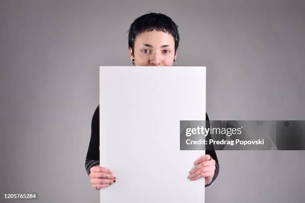 cute short haired young beautiful woman with short hair holding blank white sign on studio background - person holding blank sign stock-fotos und bilder