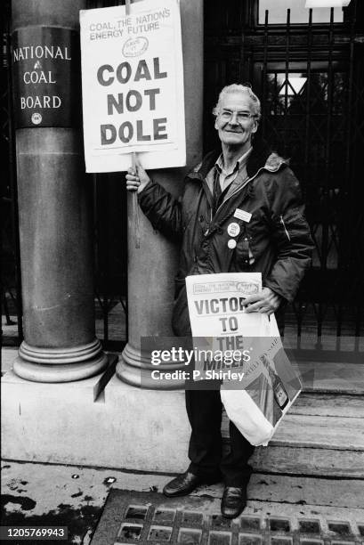 Protester holding placards saying 'Coal Not Dole'and 'Victory To The Miners' on the miners' strike picket outside the headquarters of the National...