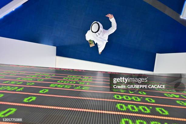 Trader walks by beneath a stock display board at the Dubai Stock Exchange in the United Arab Emirates, on March 8, 2020. - Saudi's stock exchange...