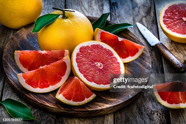 whole and sliced grape fruit shot on rustic wooden table - grapefruit stock pictures, royalty-free photos & images