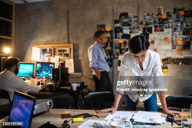 police woman working late alongside her colleagues to solve murder case late at night at office - detective badge stock pictures, royalty-free photos & images
