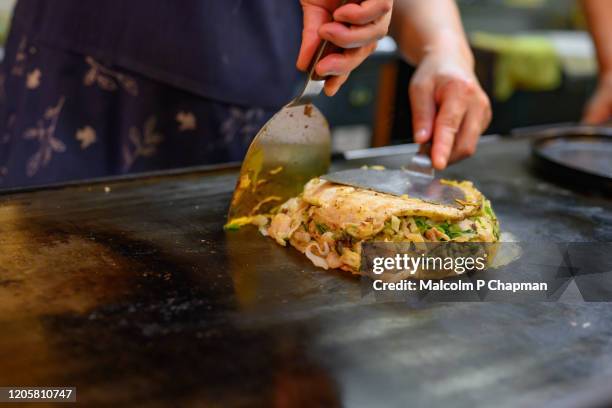 making okonomiyaki, a kansai dish particularly from hiroshima, cooked on a griddle with cabbage, shrimp, bacon and noodles. - gusseiserne pfanne stock-fotos und bilder