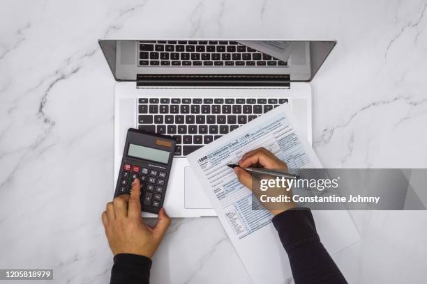 overhead view of hand filling up tax form and using calculator and laptop - income tax fotografías e imágenes de stock