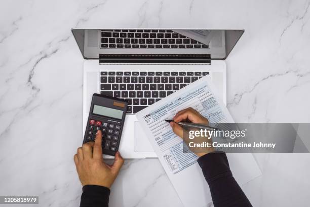 overhead view of hand filling up tax form and using calculator and laptop - tax form photos et images de collection