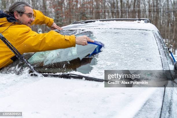 reife langhaarige mann reinigung auto windschutzscheibe von schnee und eis nach einem schneefall - beschlagen stock-fotos und bilder