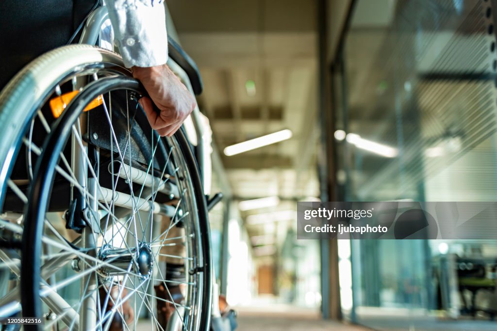 Vista posteriore di una persona irriconoscibile su una sedia a rotelle in un corridoio
