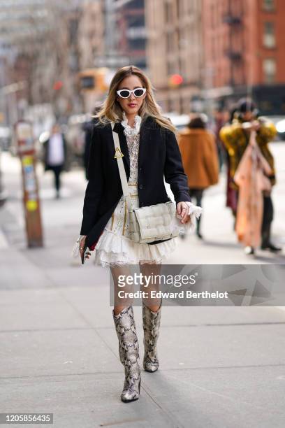 Rosa Crespo wears white sunglasses, a black jacket, a white quilted bag from Bottega Veneta, a white lace mesh ruffled dress, gray snake pattern...