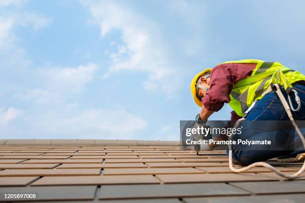 construction workers fixing roof tiles, with roofing tools, electric drills used on roofs in safety kits for safety. - dakdekker stockfoto's en -beelden
