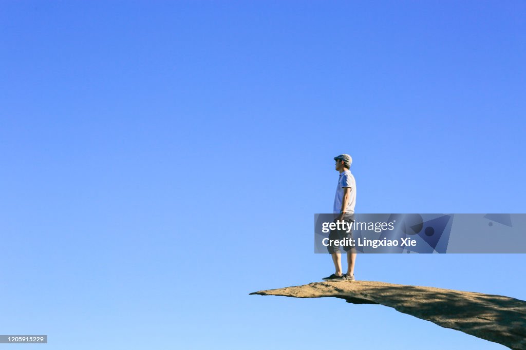 Man standing on Potato Chip Rock against blue sky, Mt. Woodson Summit, California
