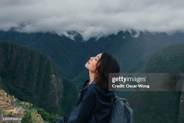 young woman enjoying fresh air on the mountain of machu picchu in peru - fresh air breathing stockfoto's en -beelden