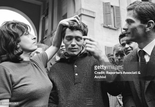 Italian actress Anna Magnani touching Italian actor Franco Citti's hair in front of Italian director and writer Pier Paolo Pasolini at the premiere...