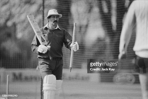 English cricketer Graham Gooch carrying a stump and a cricket bat, and wearing a bucket hat during a practice session in the nets in Essex, England,...