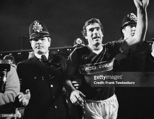 British footballers Trevor Brooking leaves the field, escorted by two police officers, after he had played his final game for West Ham in their First...