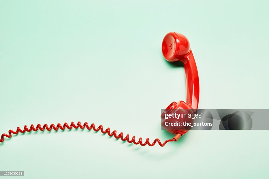 High angle view of a red old-fashioned telephone receiver with a coiled cable on turquoise background