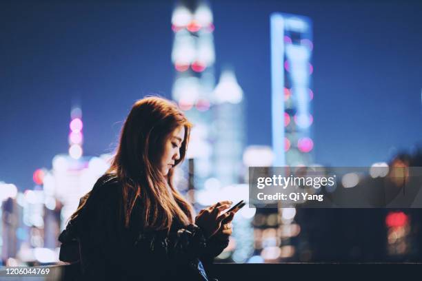 young woman standing on rooftop using smartphone - shanghai calling stock pictures, royalty-free photos & images