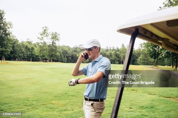 young man using mobile phone on golf course - ポロシャツ ストックフォトと画像