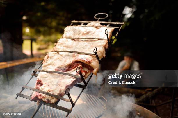rib barbecue being prepared with elderly man sitting in the background - gaucho stock pictures, royalty-free photos & images