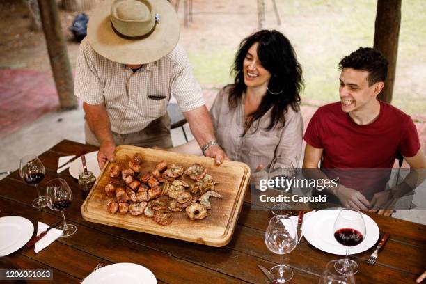 senior man offering barbecue to family at country house - churrasco - gaucho argentina stock pictures, royalty-free photos & images