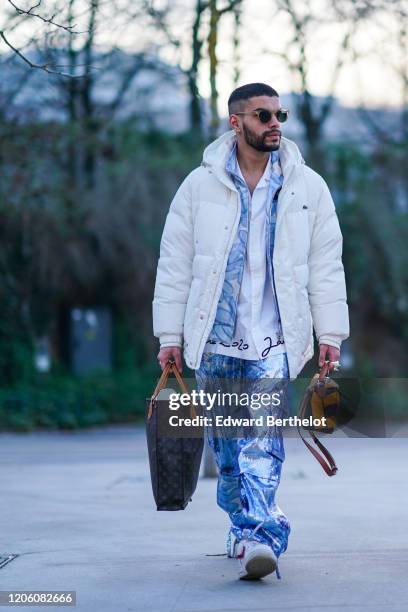 Guest wears sunglasses, a Jacquemus Coup de Soleil white shirt, a blue and white floral print jacket, a white Lacoste padded jacket, glittering...