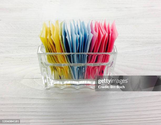 sugar substitute packets in a glass container on a white, painted wood surface - artificial sweetener - part of a series - sachet stockfoto's en -beelden