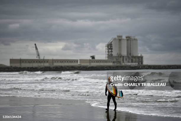 This photo taken on March 4, 2020 shows Koji Suzuki, a surfer and a surf shop owner, walking on the beach in front of a thermal power station after a...