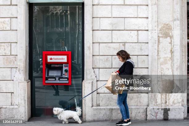 Pedestrian walks a dog past an automated teller machine outside a Banco Santander SA bank branch in Barcelona, Spain, on Friday, March 6, 2020....