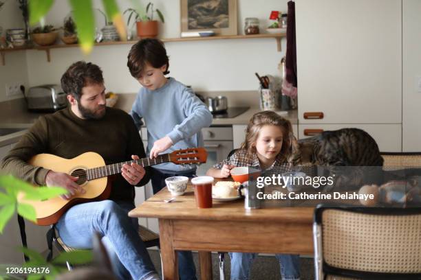 a father playing guitar with his children during the breakfast - hipster in a kitchen stock-fotos und bilder