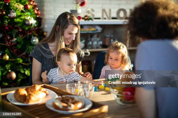 young family with two kids sitting at dining table and enjoying christmas day together - christmas breakfast stock pictures, royalty-free photos & images