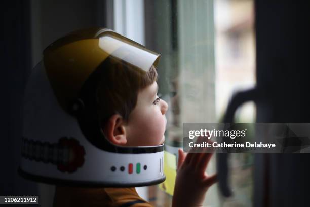 a four year old boy wearing a cosmonaut helmet, looking out the window - menino a sonhar imagens e fotografias de stock