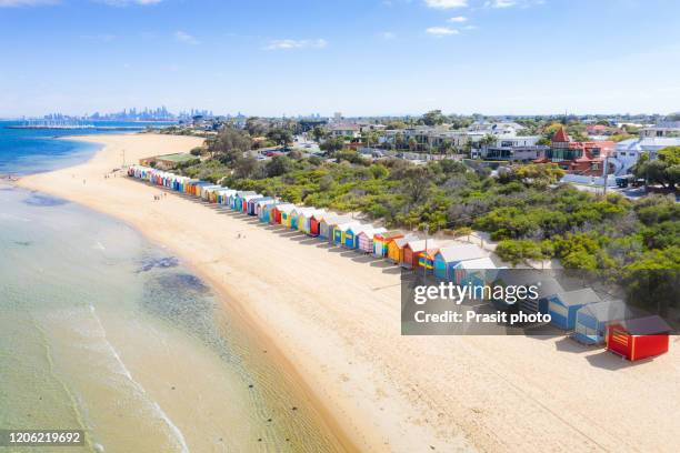 aerial view of colorful brighton bathing boxes on white sandy beach at brighton beach with city in background in melbourne, victoria, australia. - aerial melbourne fotografías e imágenes de stock