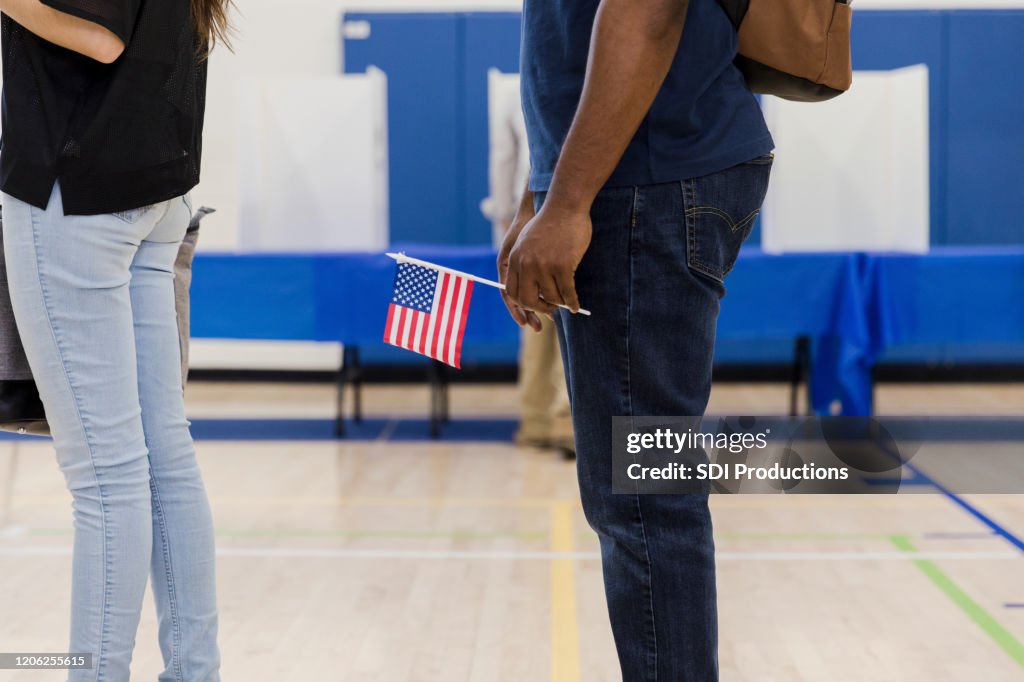 Unrecognizable man holds US flag while waiting to vote