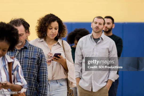 woman uses phone while waiting to vote - woman waiting in line stock pictures, royalty-free photos & images