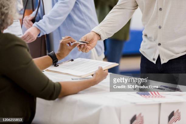 volwassen vrouwelijke opiniepeilingsplaatsvrijwilliger helpt kiezer - polling place stockfoto's en -beelden