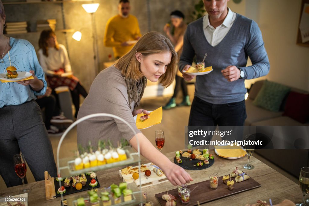 Beautiful young woman taking food during after work dinner party