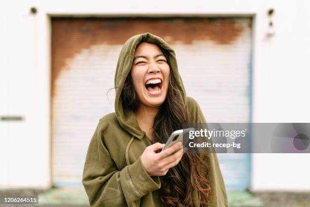 retrato de la mujer joven sosteniendo el teléfono inteligente y riendo - women laughing fotografías e imágenes de stock