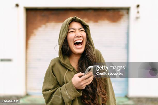 portrait of young woman holding smart phone and laughing - asiático e indiano imagens e fotografias de stock