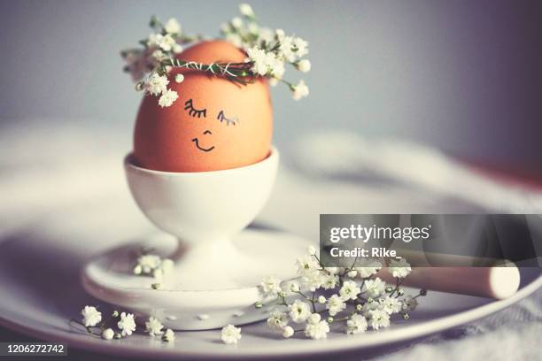 natural easter egg in an eggcup with funny painted face and sweet flower wreath on easter breakfast - easter breakfast stock pictures, royalty-free photos & images