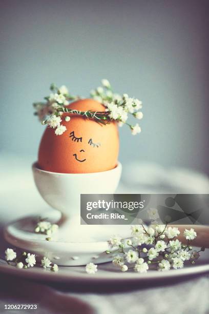 natural easter egg in an eggcup with funny painted face and sweet flower wreath on easter breakfast - easter breakfast stock pictures, royalty-free photos & images