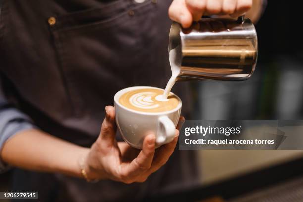 close up view of young woman preparing a coffee by drawing a flower with milk - barista foto e immagini stock