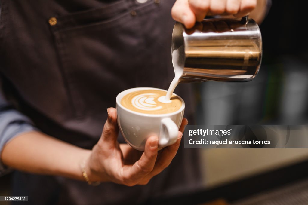 Close up view of Young woman preparing a coffee by drawing a flower with milk