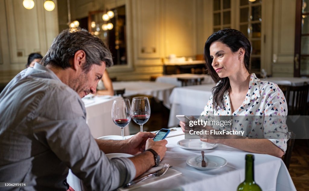 Disappointed married couple text messaging while having dinner