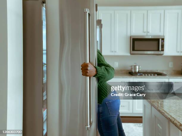 woman looks into refrigerator for healthy snack - refrigerator stock-fotos und bilder
