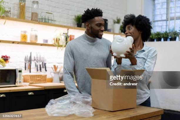 african american couple getting a piggybank in the mail at home - couple saving piggy bank stock pictures, royalty-free photos & images