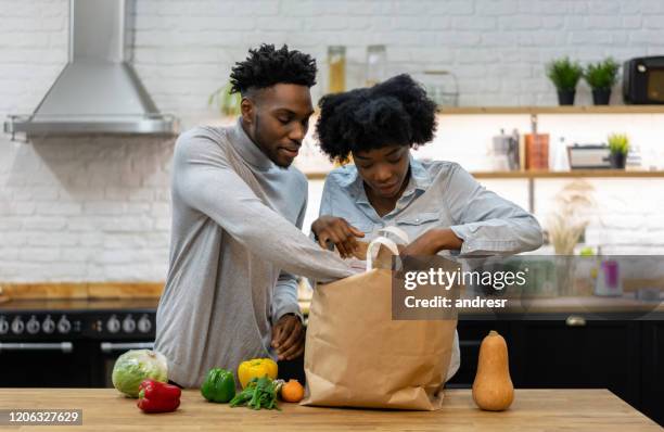 gelukkig afrikaans amerikaans paar thuis dat de boodschappen uitpakt - young man groceries kitchen stockfoto's en -beelden