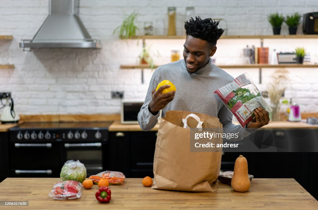 Feliz hombre afroamericano en casa desempaquetando los comestibles