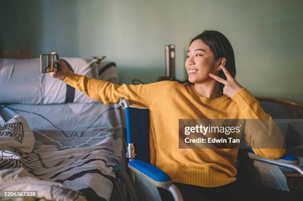 a disable asian chinese teenager girl having selfie on her wheelchair in hospital ward recovering from her illness - girl in hospital bed sick stock pictures, royalty-free photos & images