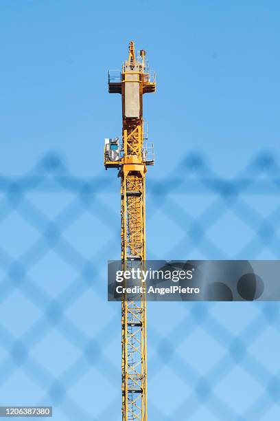 yellow crane at the other side of the fence - grúa stock pictures, royalty-free photos & images