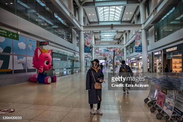 Traveler is seen wearing a rain suit, facemask, and protective plastic over her head to protect herself from COVID-19 while waiting for her flight...