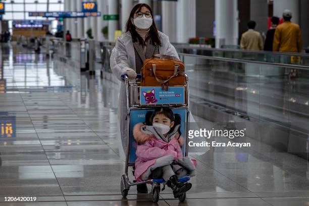 Traveler and her child are seen wearing raincoats and facemasks to protect themselves from COVID-19 while waiting for their flight inside Incheon...